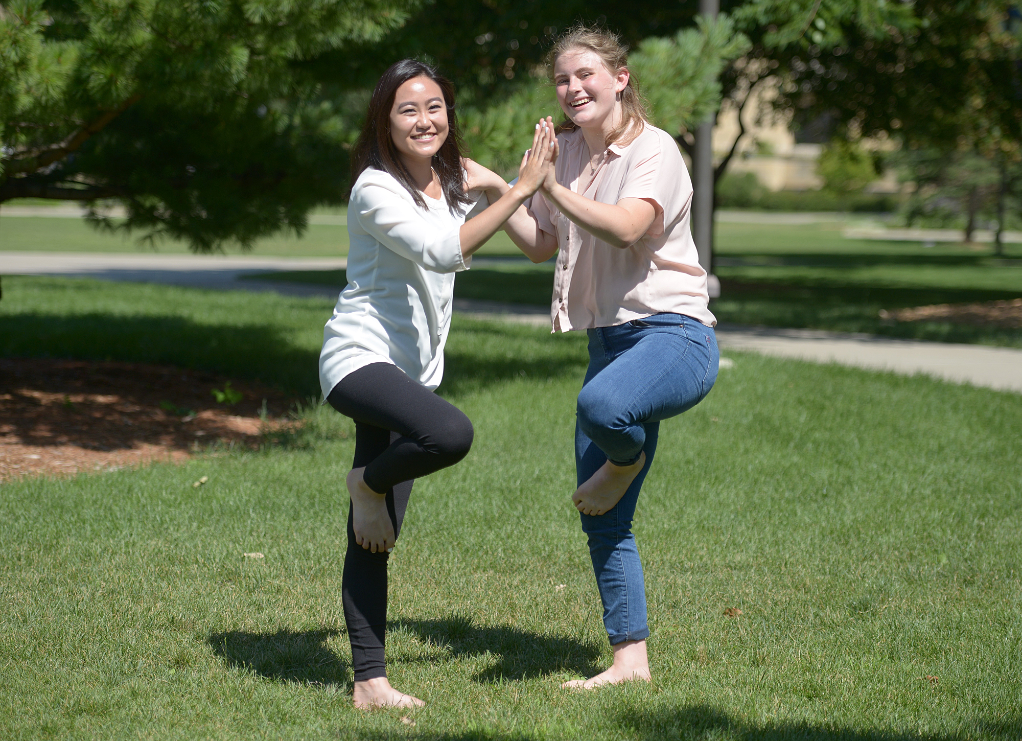 two women performing yoga in a park